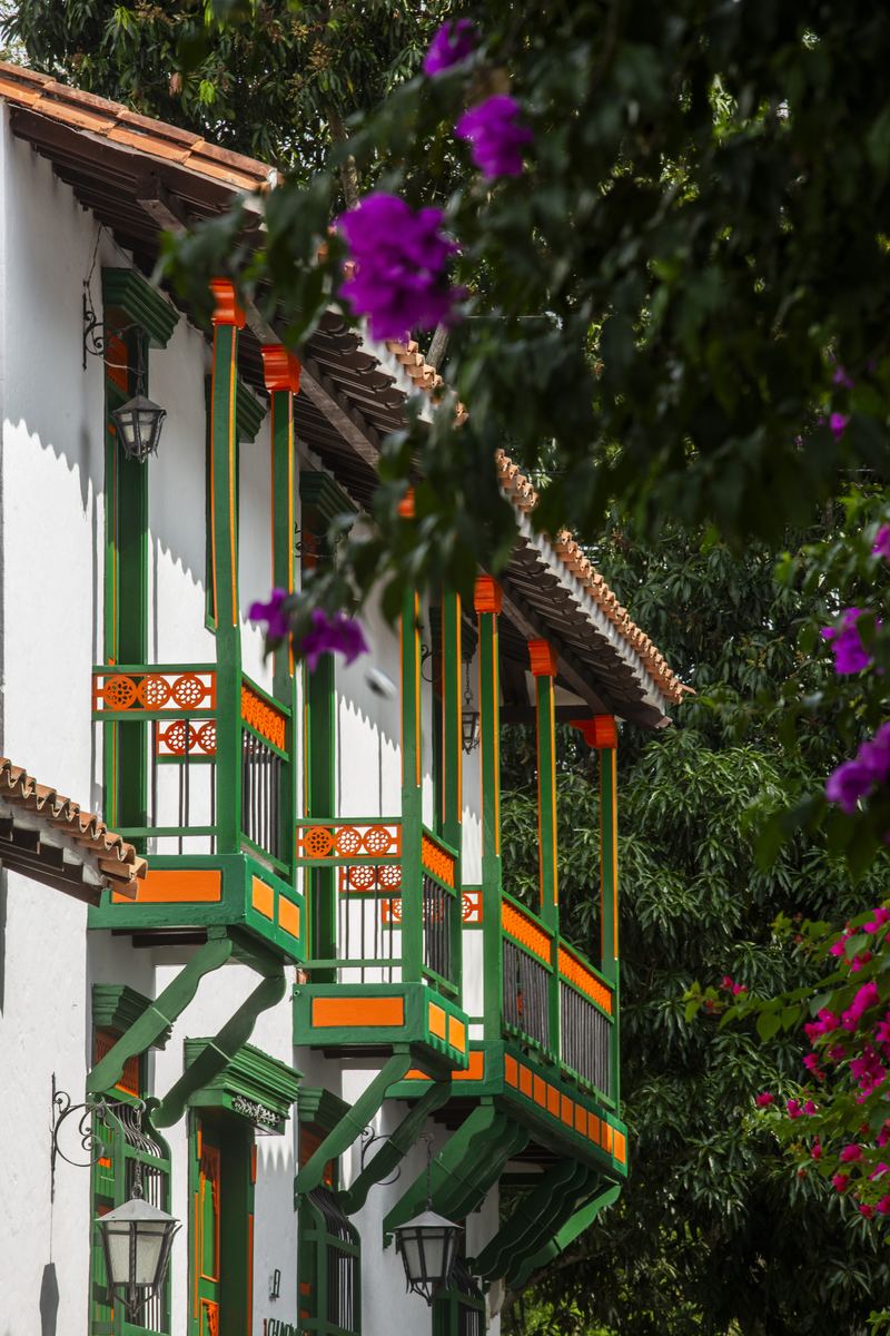 Balcones de madera pintados de verde, rojo y naranja, con flores, en una calle de Cauca Viejo