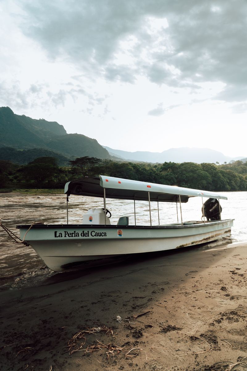 La lancha varada en la playa del río Cauca, con el agua y las montañas detrás
