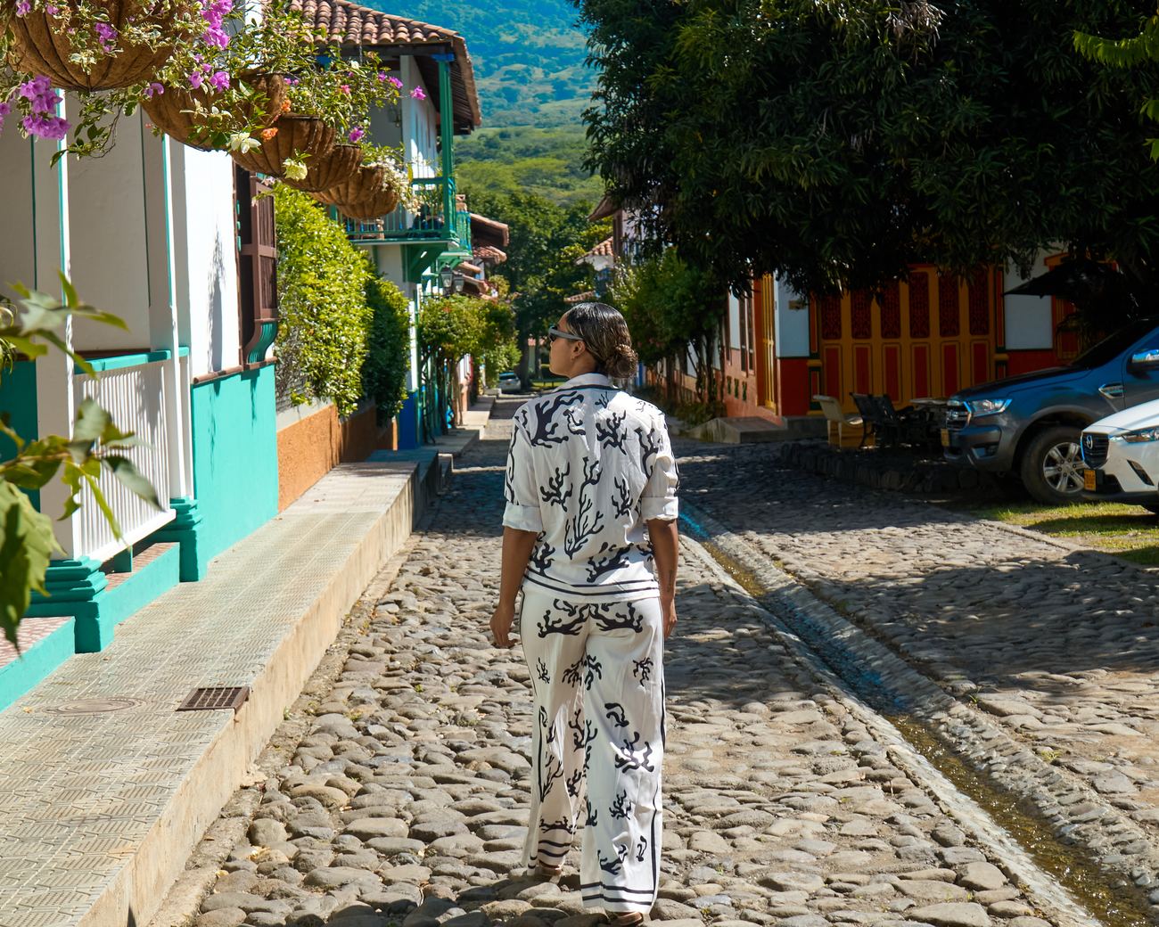Una persona camina por la calle empedrada de Cauca Viejo entre casas de balcones con flores