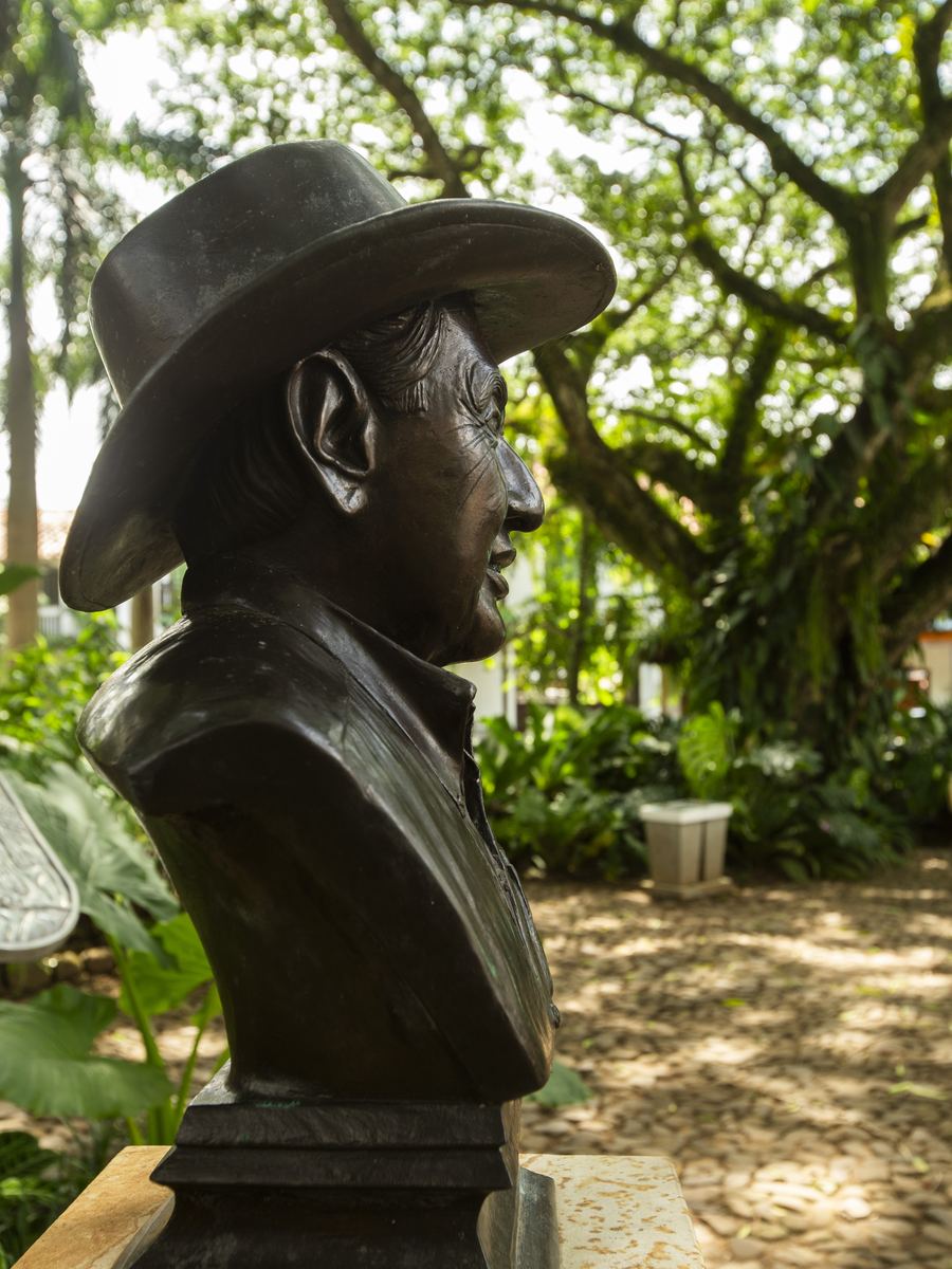 El busto del fundador, con sombrero, entre las plantas del parque