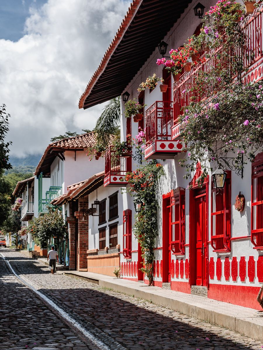 Una calle empedrada con casas blancas de balcones rojos llenos de flores
