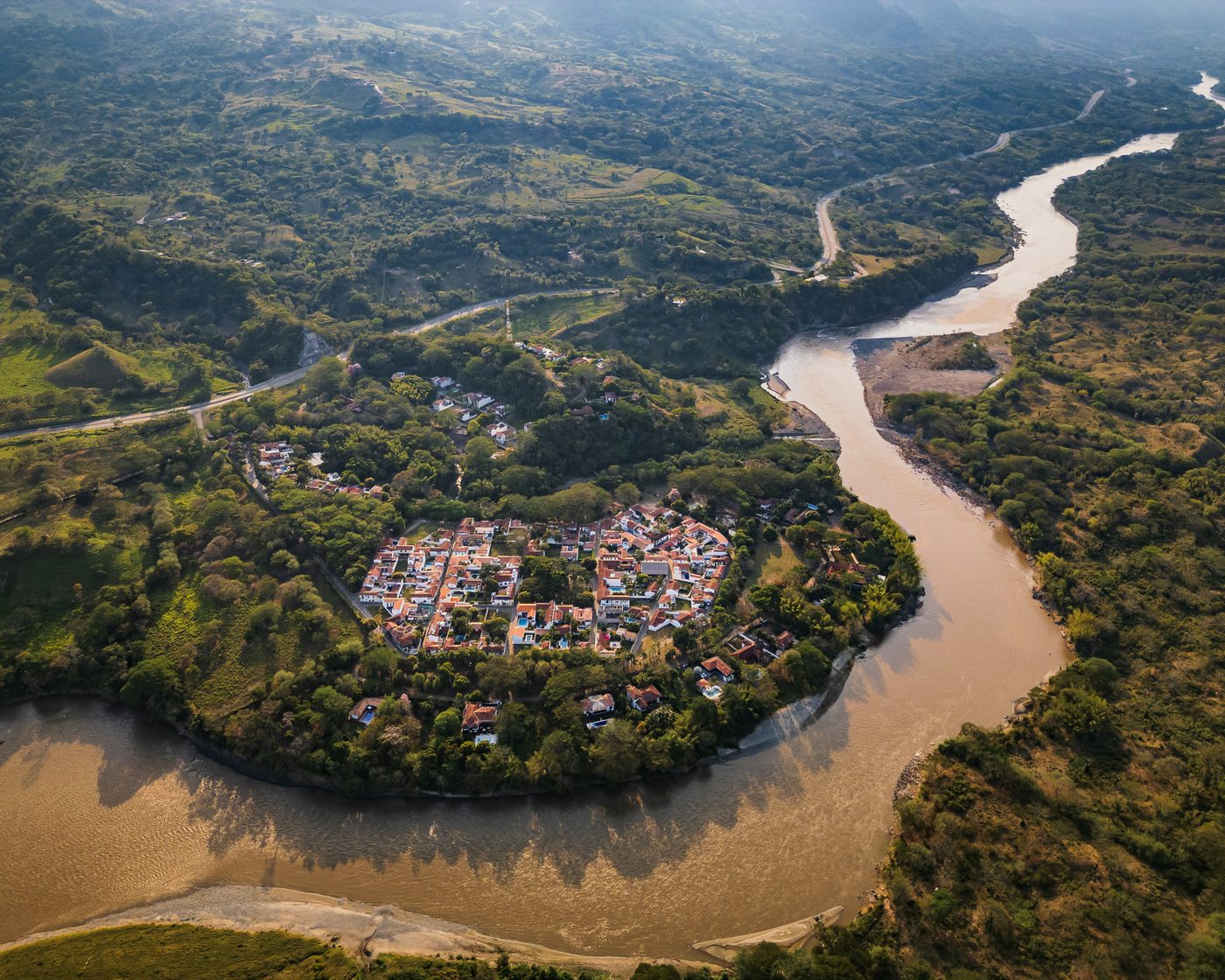 El pueblo entero en la curva del río Cauca, visto desde el aire, con las montañas detrás